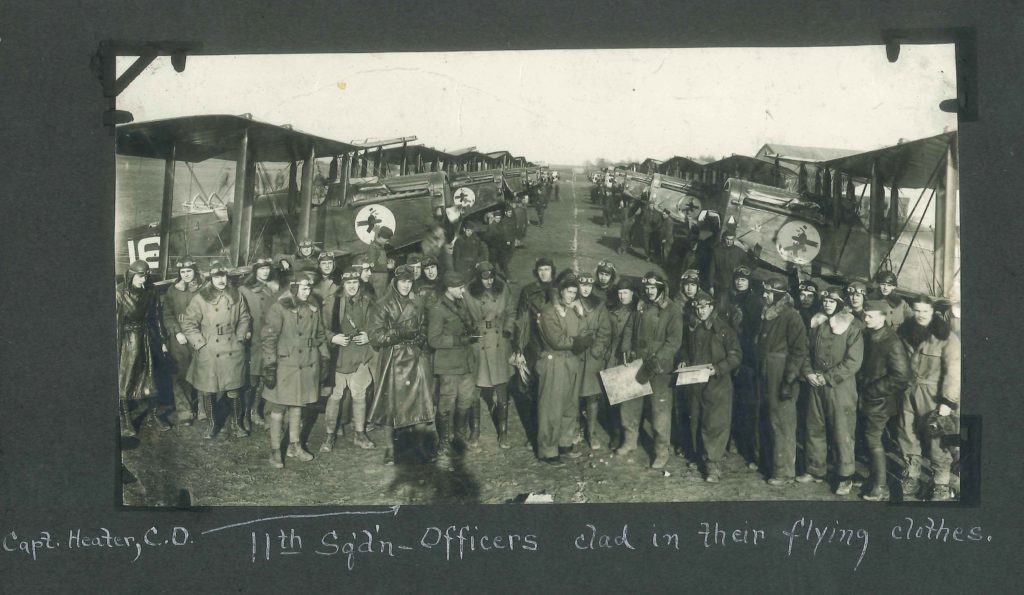 Officers in flying clothes arrayed informally in front of a two receding lines of DH-4s.