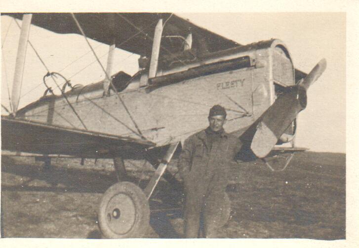 A man dressed in a mechanic's suit standing next to the propeller of a DH-4 that has "Fleety" painted on it.