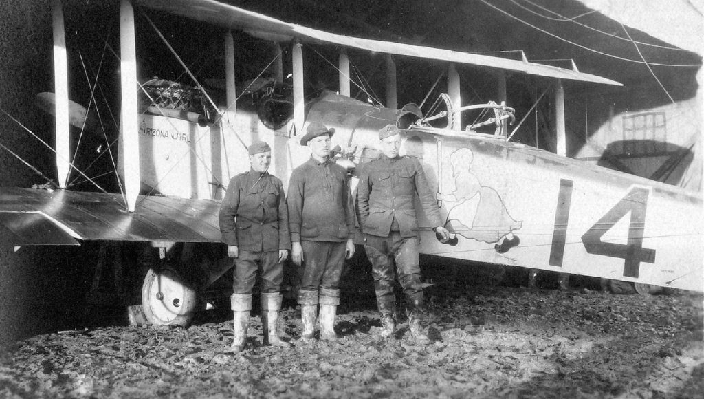 A photo of three men standing in front of plane that has the number 14 on it.