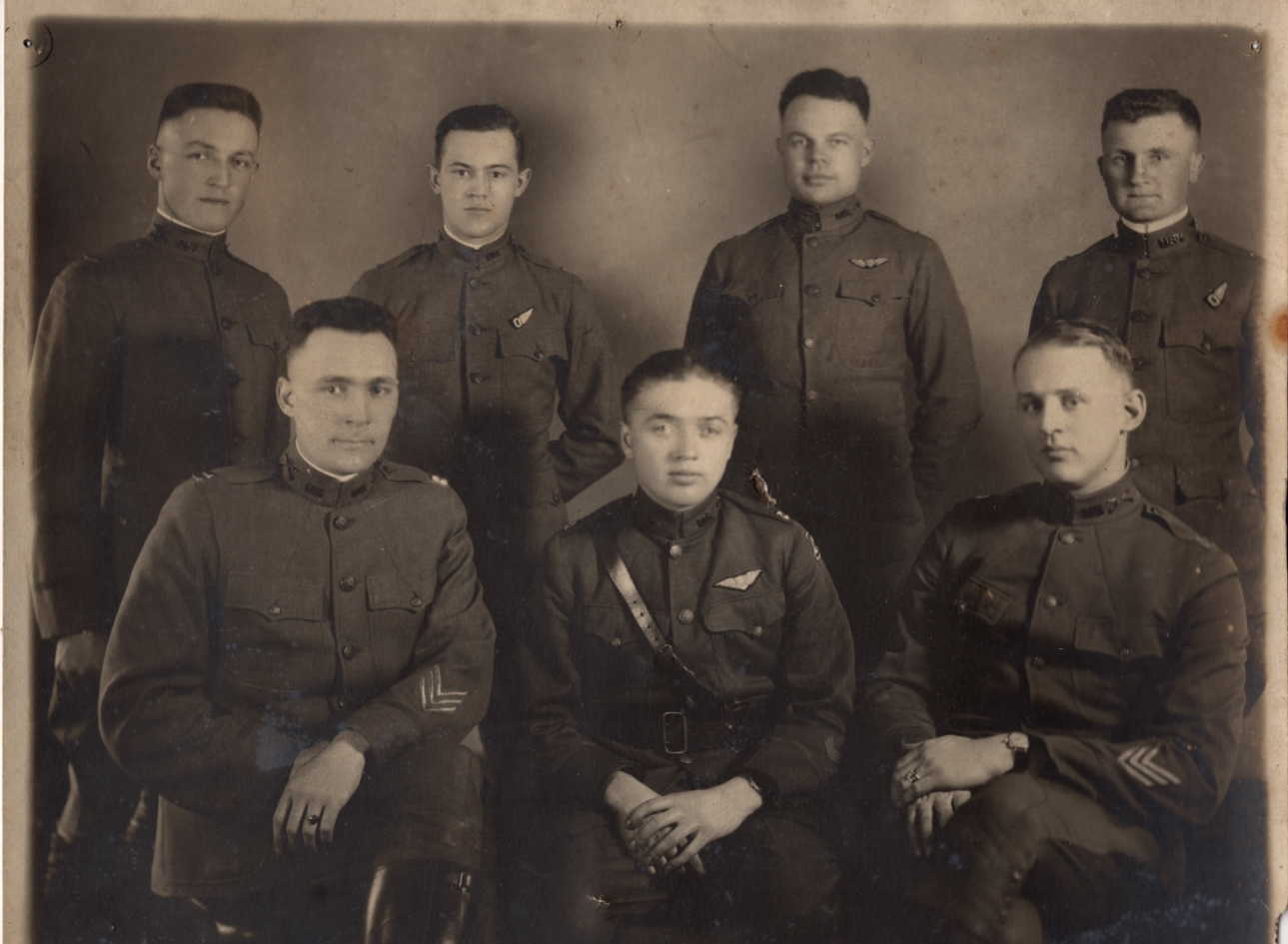 A photo of seven men in uniform, four standing and three seated.