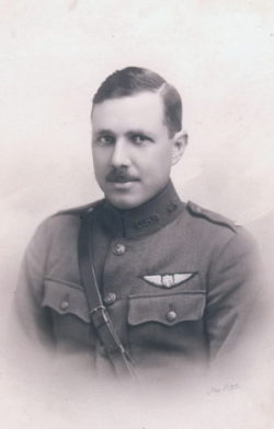 Formal portrait, head and shoulders, of a hatless young man in uniform, wearing a Sam Browne belt, with a pilot's wings above his left pocket.