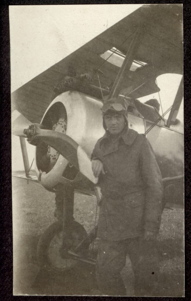 Photo of man in flying helmet with goggles standing in front of a Sopwith Camel.