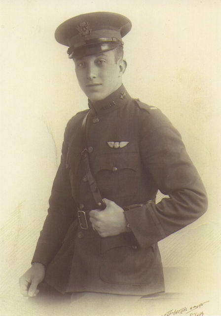 Three quarter formal studio photo of young man in uniform with pilot's wings over his left breast pocket and wearing a peaked officer's cap.