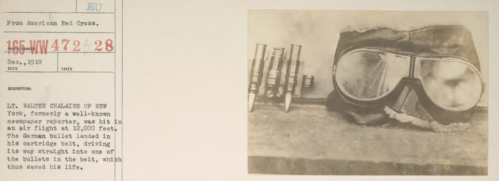 A photo of four bullets from a cartridge belt next to a pair of aviator goggles pasted onto a piece of archives paper with the notation "from American Red Cross," a catalogue number, and a description of the photo focussed on the cartridge belt.