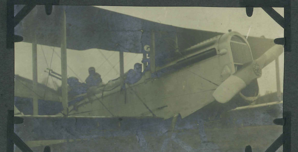 Close up photo of a DH-4 showing front of fuselage and wings, with pilot in cockpit and man behind him manning guns.