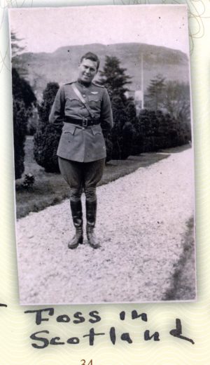 Foss in uniform, with pilot's wings above his left breast pocket, standing on what appears to be a gravel walk with a background of evergreens and a hill.