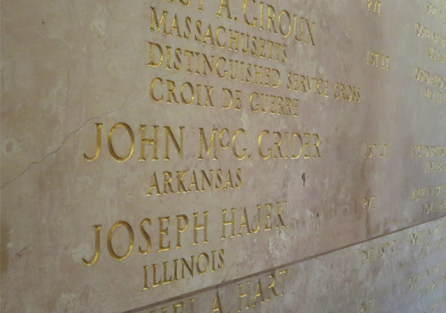 An oblique photo of a wall with names carved into it and gilded; prominent in the center is "John McG. Grider Arkansas."