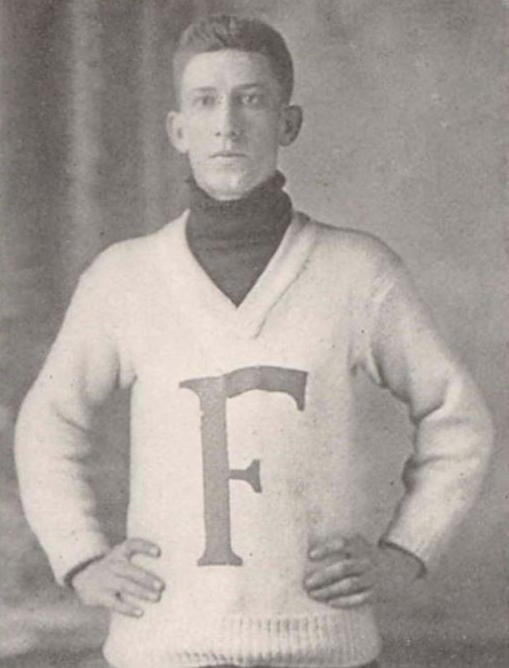 A photo from the waist up of a man wearing a white sweater with a large "F" on it.