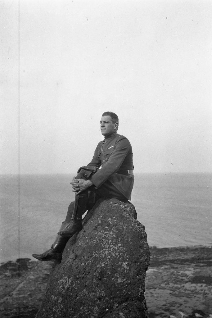 Man in uniform sitting on a rock with beach and ocean in back ground.