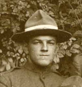 Photo of man (face and shoulders) wearing a campaign hat against a background of ivy leaves.