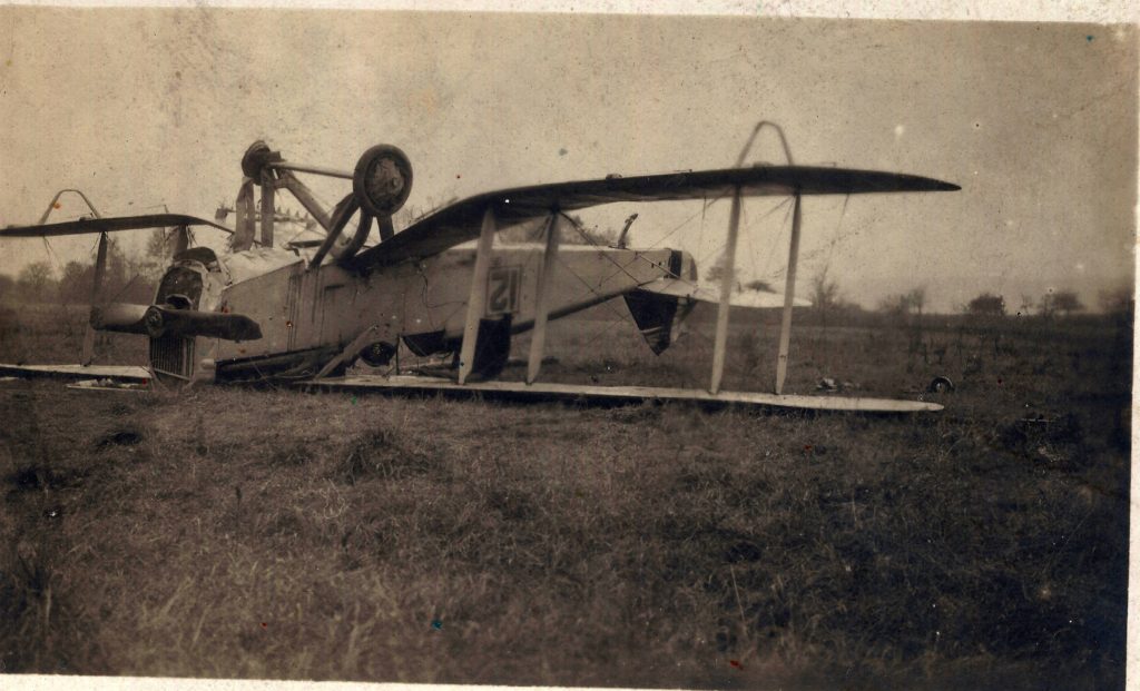 A biplane on its back in a field.