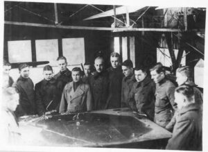 Photo of fifteen men in overcoats gathered around a table with what appears to be a large map on it.